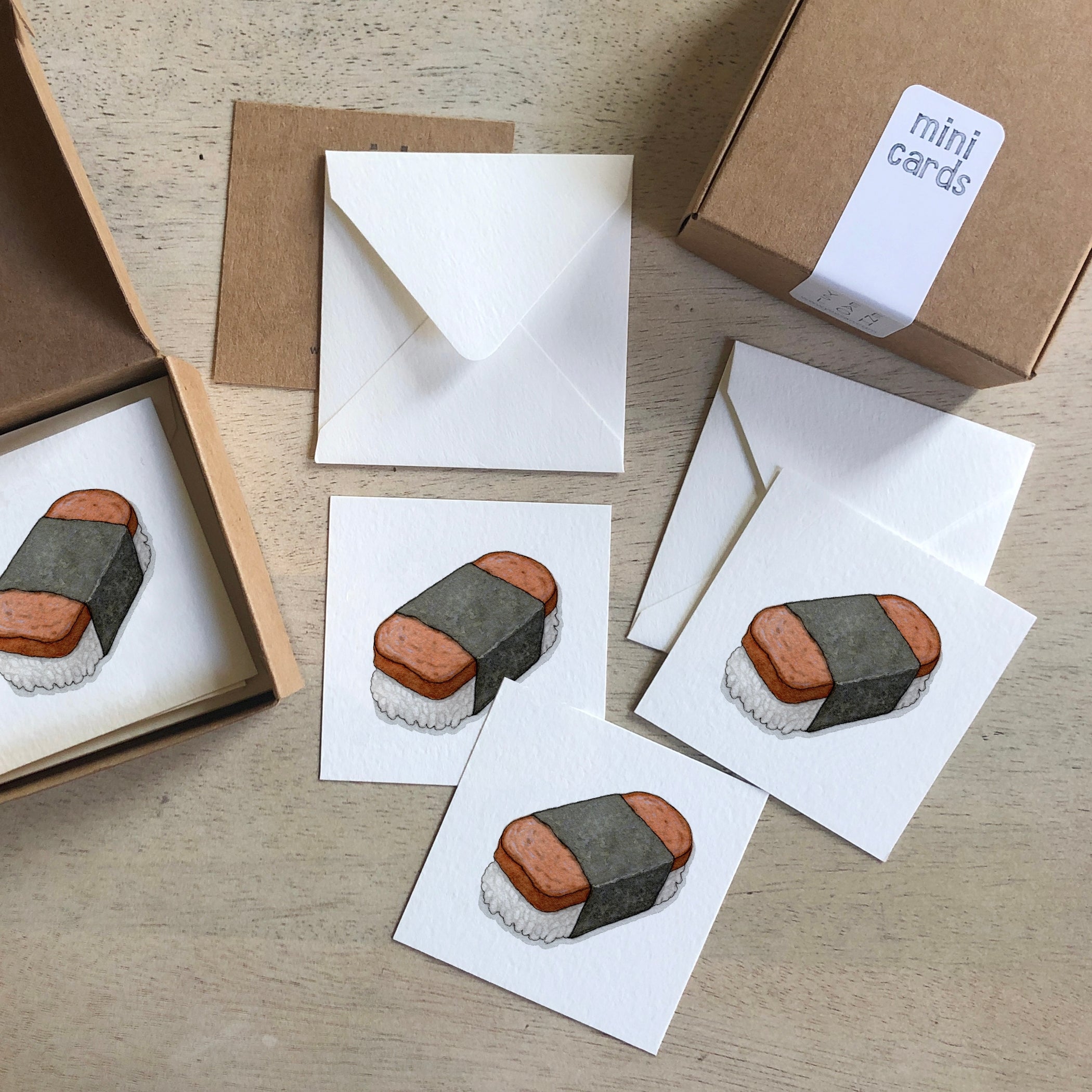 Mini cards and white envelopes with sushi musubi illustration, shown laid out