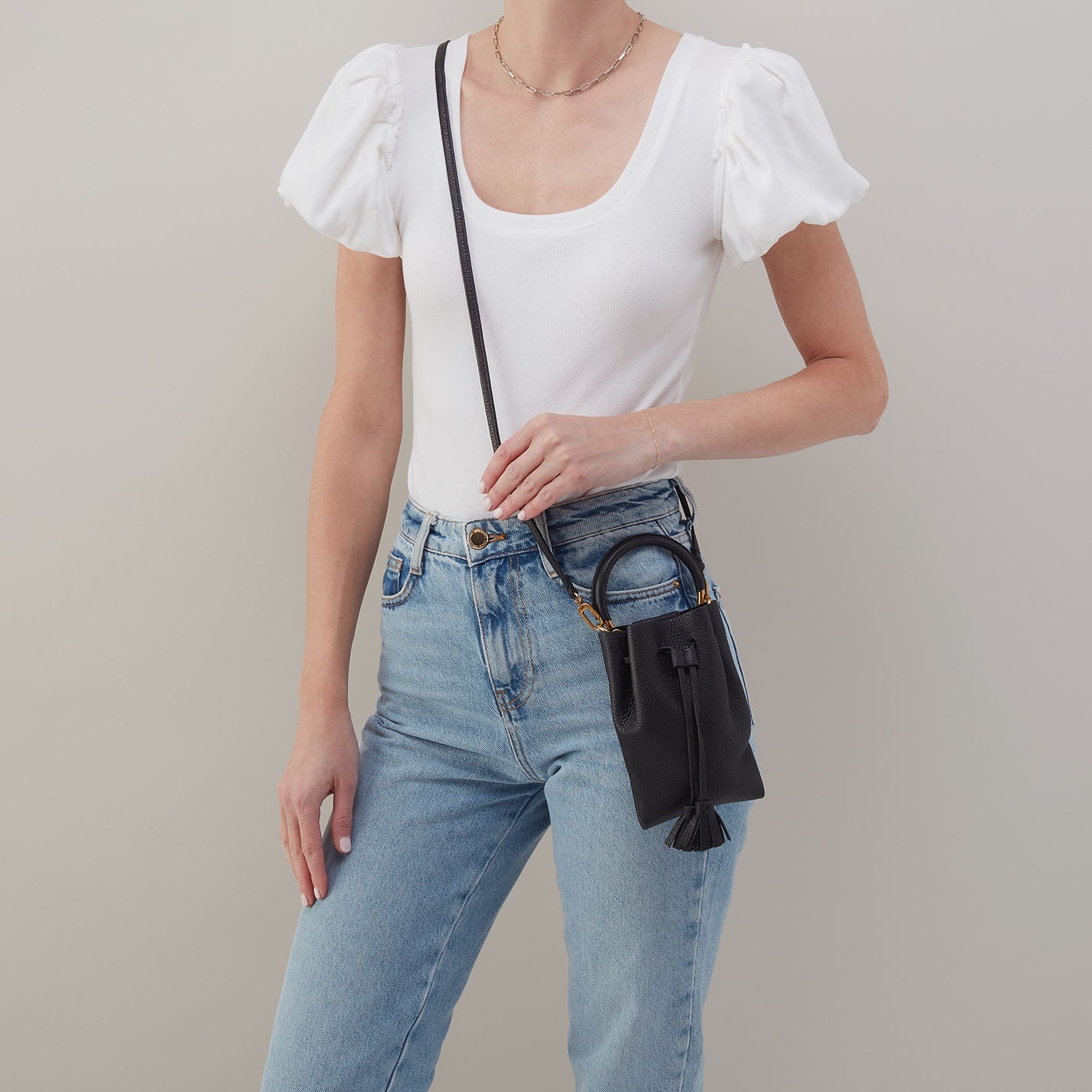 Black phone crossbody bag on model with adjustable crossbody strap and tassel charm.