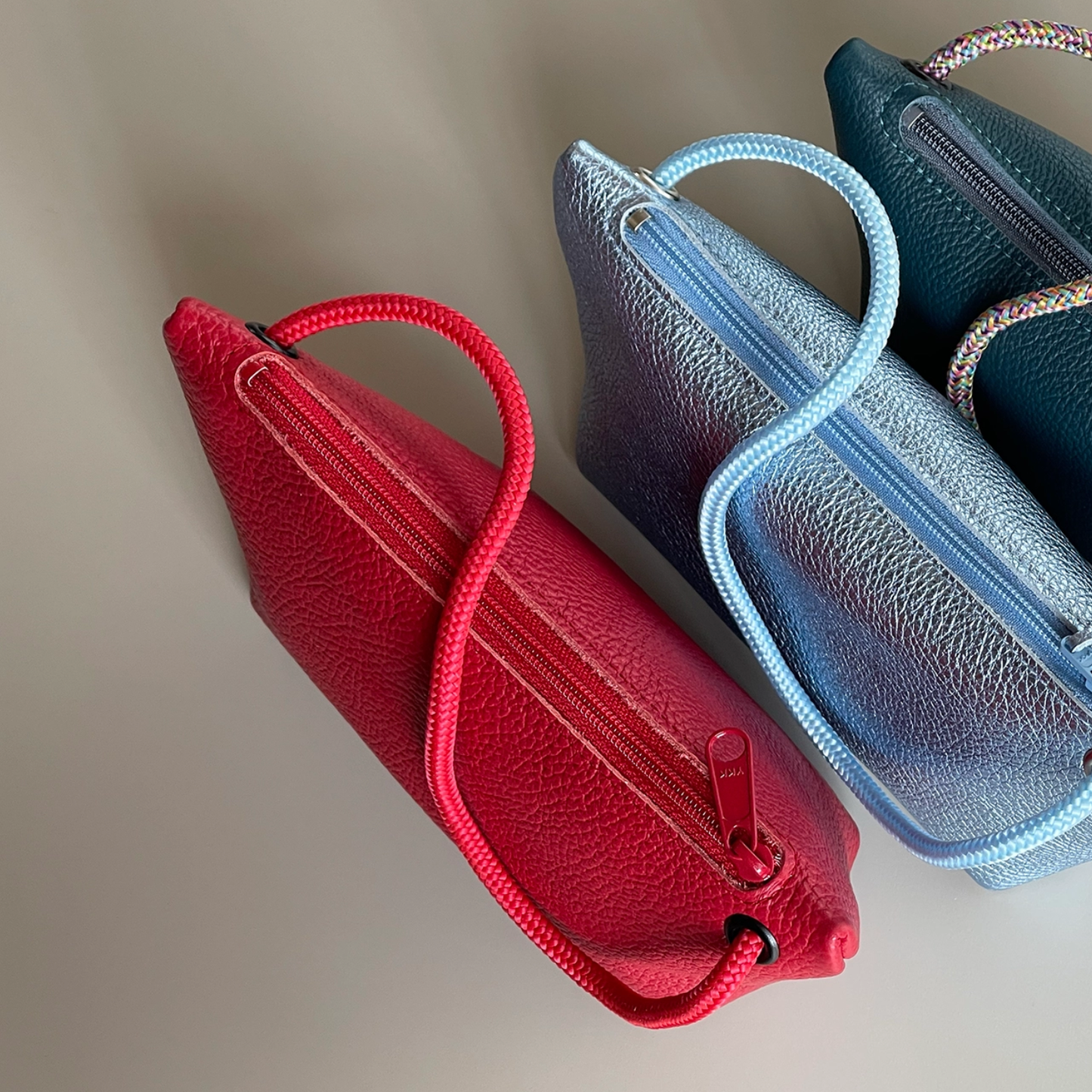 Two cord pouches, red and teal-blue, with braided handles and zipper closures.