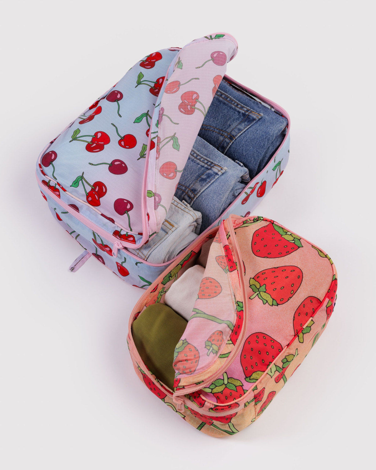 Packing cube set with strawberry print and another cube open, showing denim inside