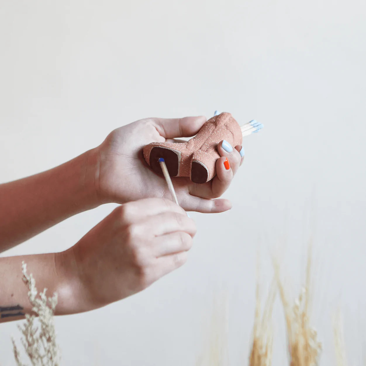 Hand holding a ceramic cowboy boot match holder with a lit match