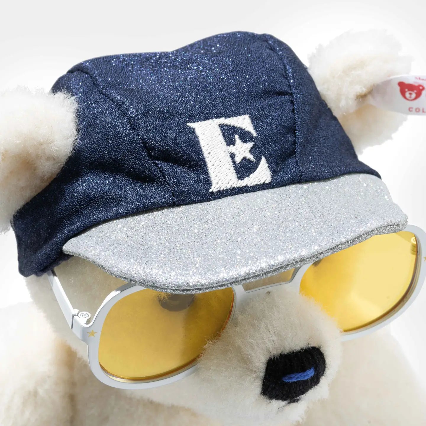 Teddy bear with navy cap, glittery brim, and round yellow-lens sunglasses