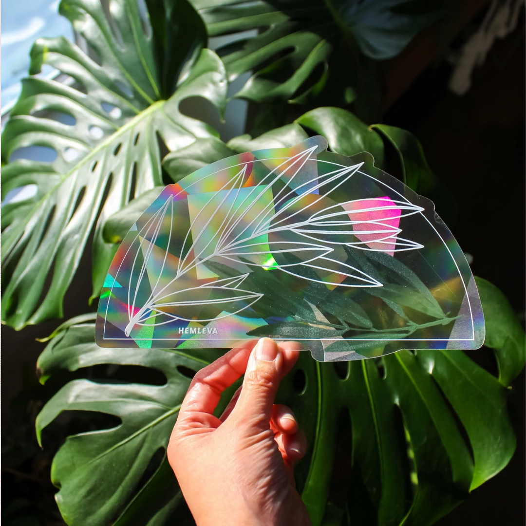 Olive-branch suncatcher with 'HEMLEVA' logo and rainbow prism light over leaf design