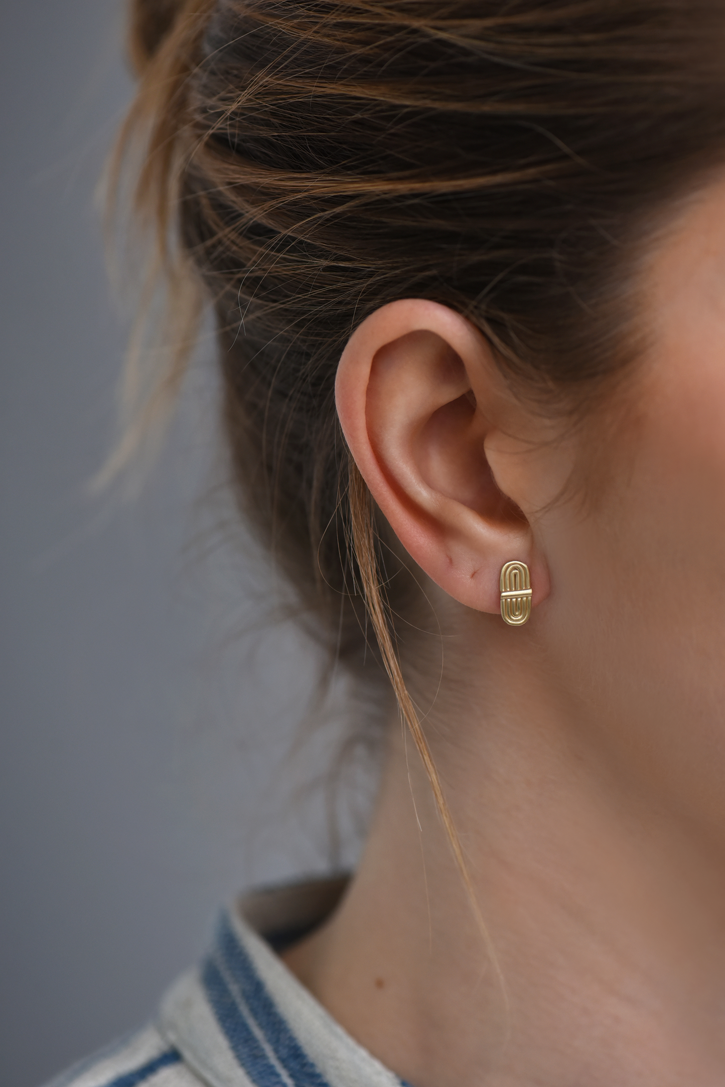 Gold-tone double-arc stud earrings on ear, curved bar front