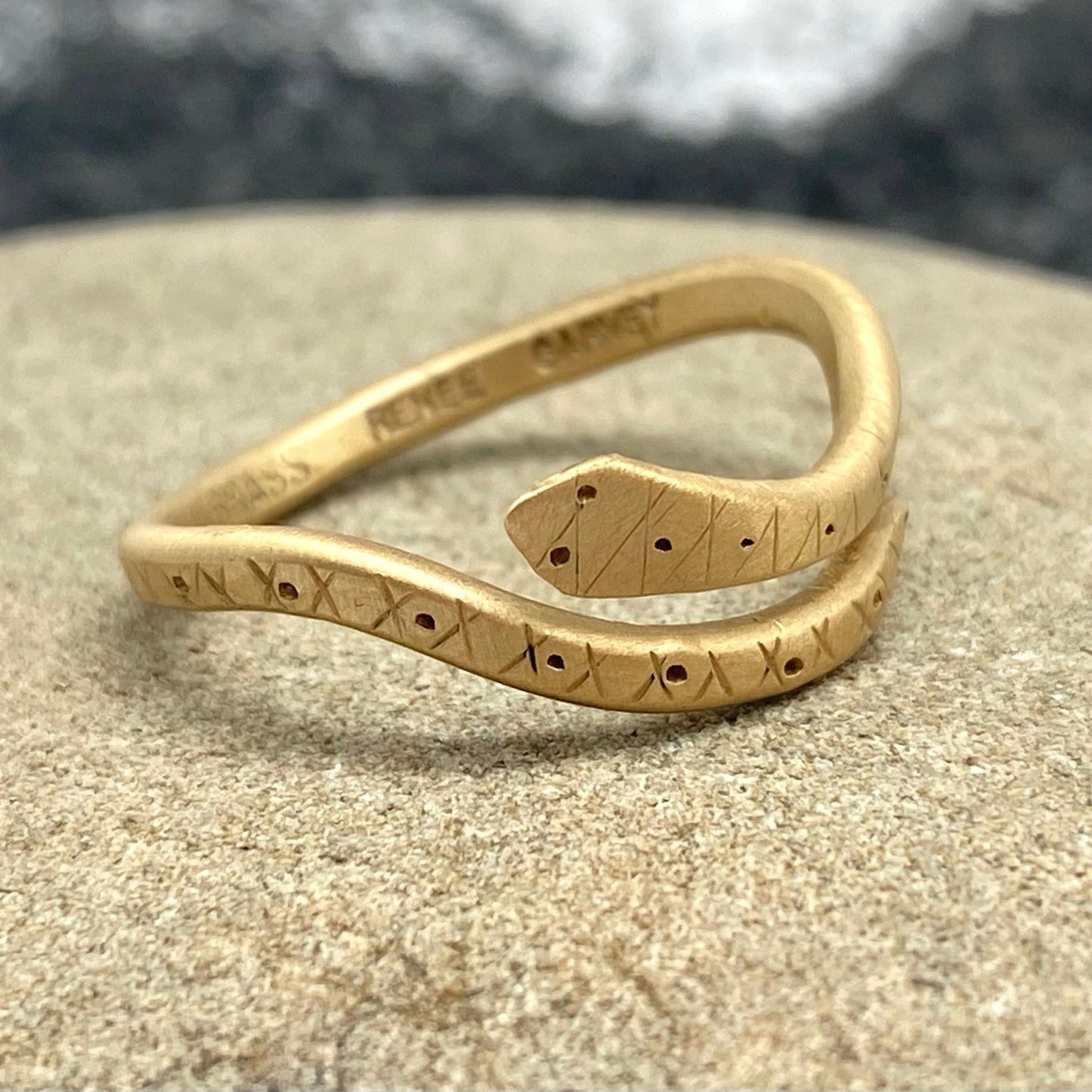 Matte brass snake ring with engraved symbol pattern, stacked close view
