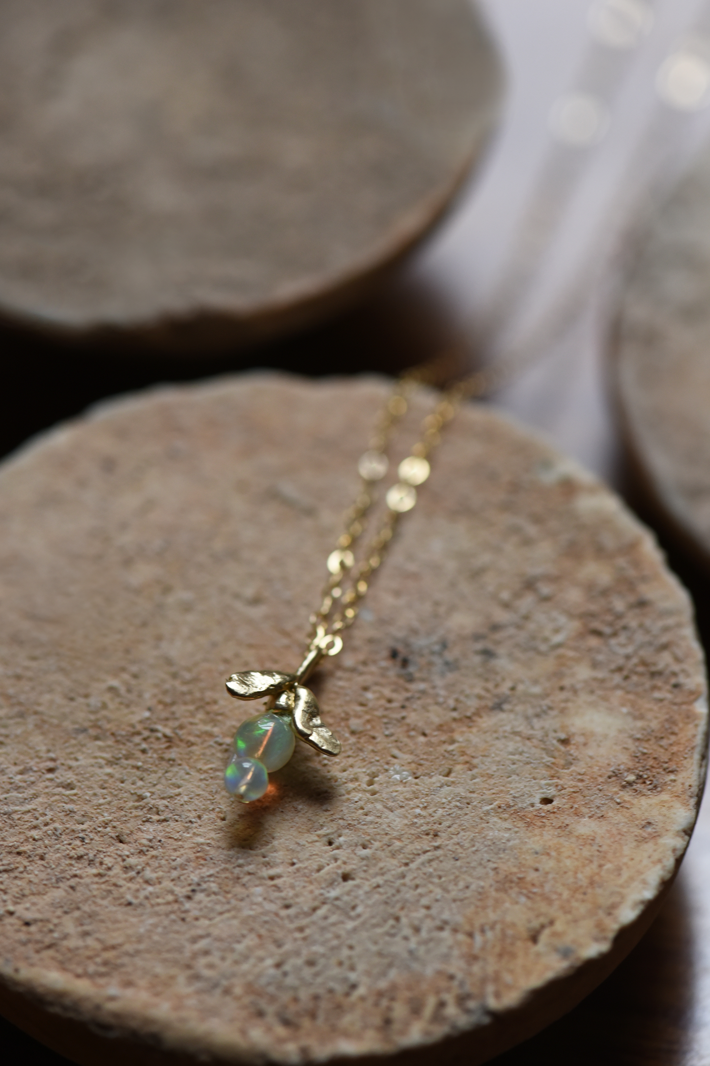 Gold chain leaf drop necklace with green opal bead pendant on a stone