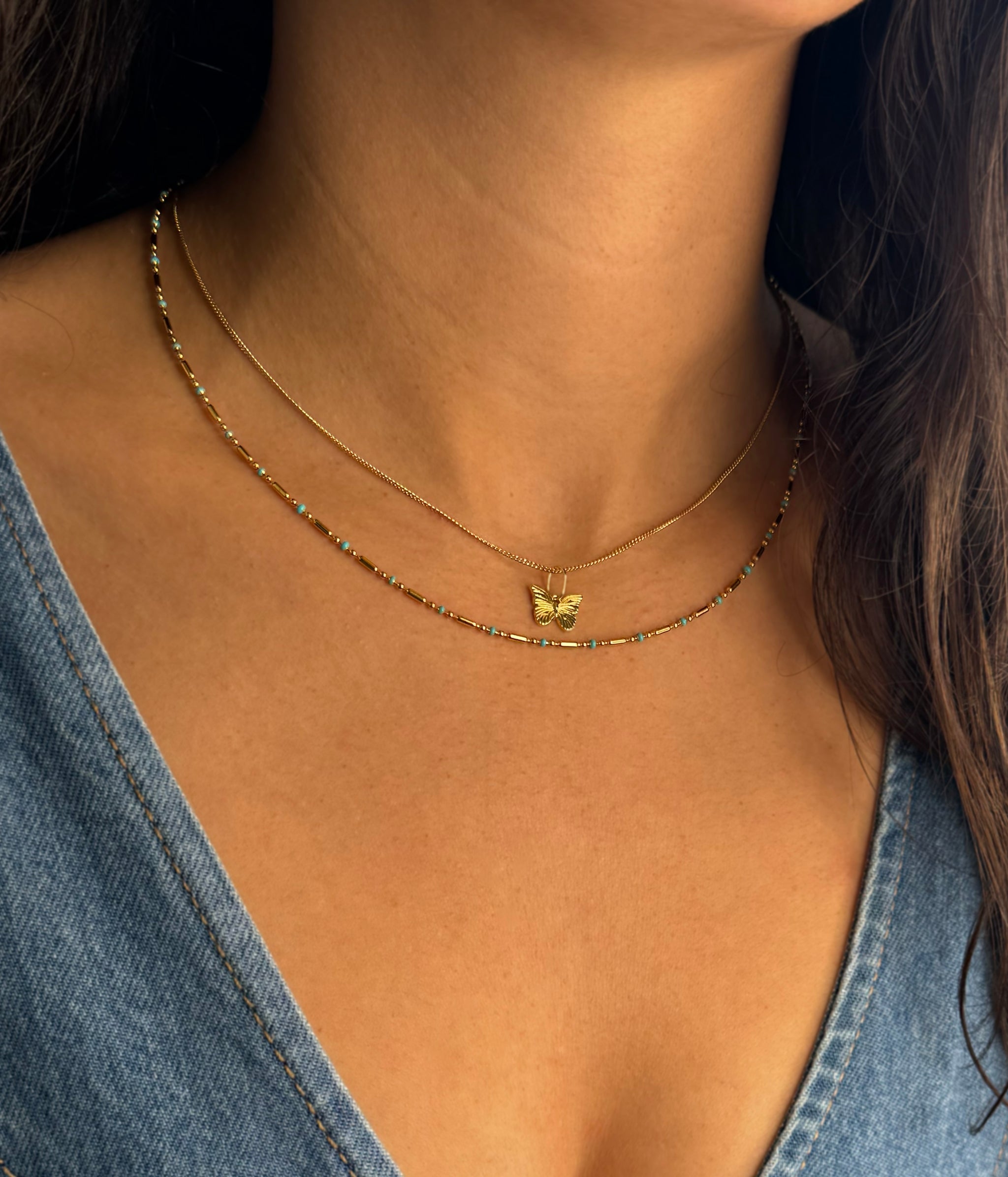 Gold butterfly charm necklace pendant on fine chain, worn at the collarbone