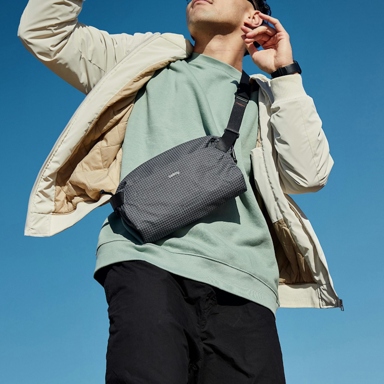 Dark gray sling bag worn crossbody with adjustable strap and zip closure