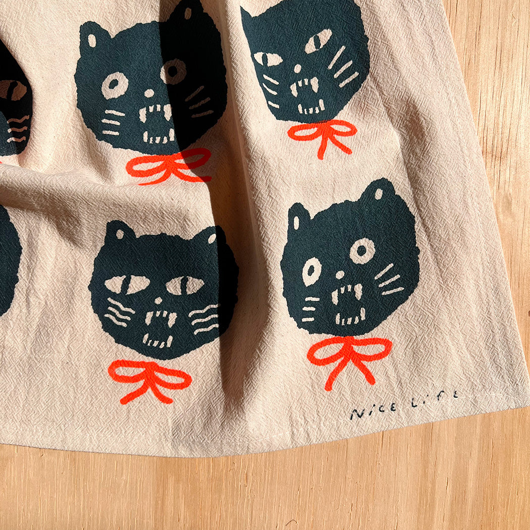 Tea towel with several dark cat faces and red bows, fabric texture visible