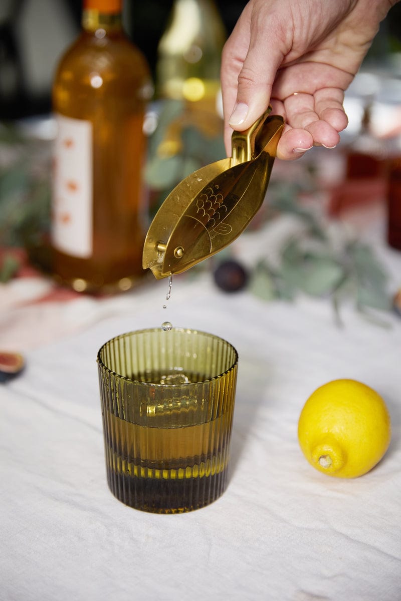 Olive green lowball glass on table as hand tips gold scoop
