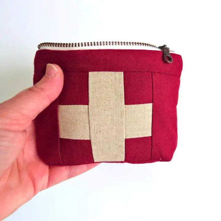 Red first aid kit pouch with cream cross patch and zipper; held by hand