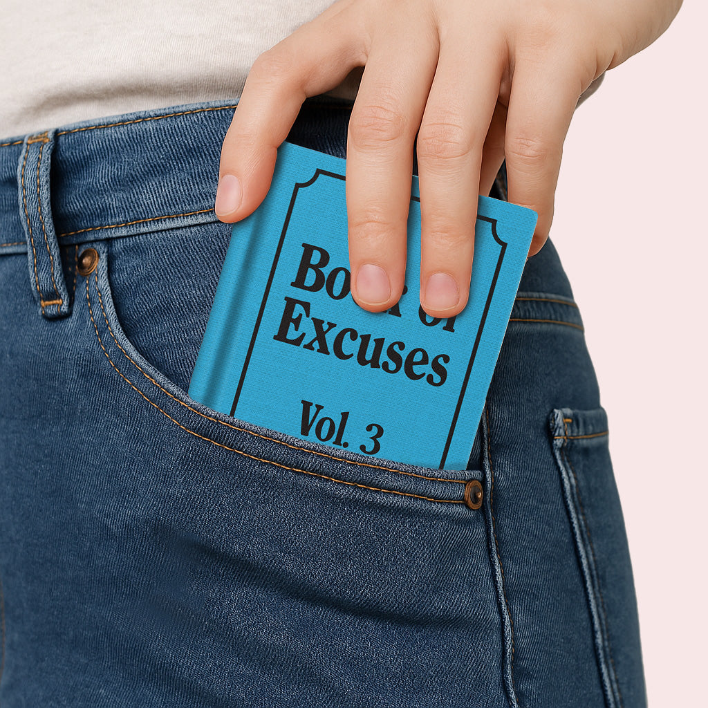 Hardback notebook held in jeans pocket; blue cover with Book of Excuses Vol. 3