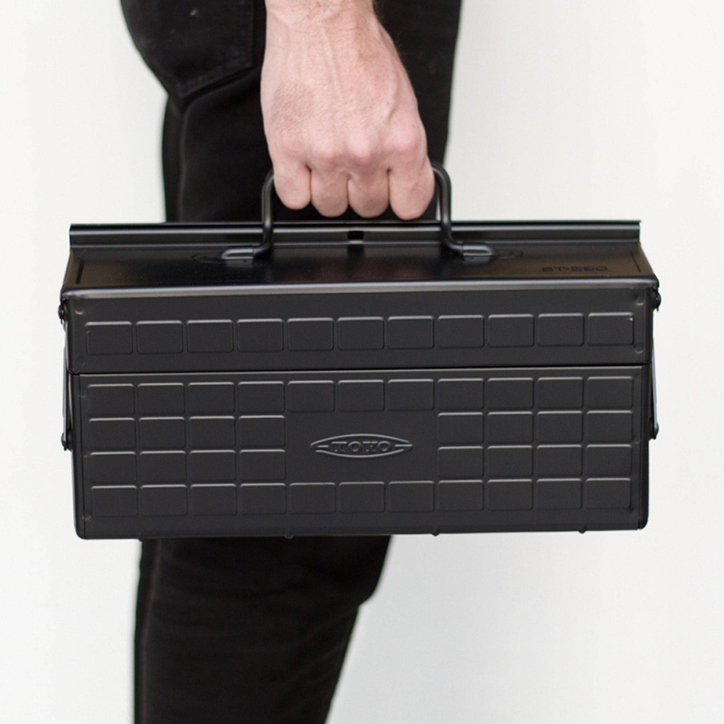 Black steel cantilever toolbox with top handle, held by hand.