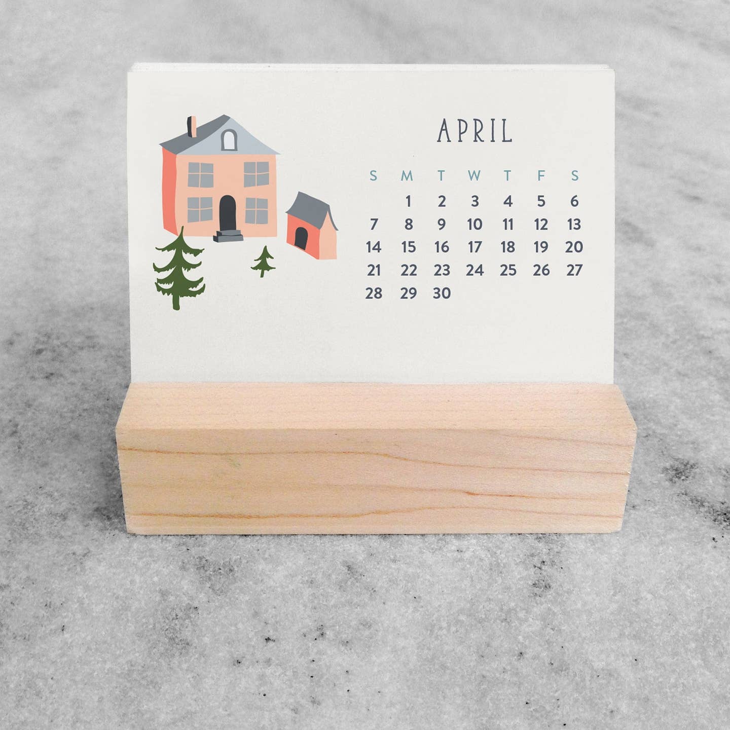 Mini desk calendar showing April, village houses and trees, wooden stand base