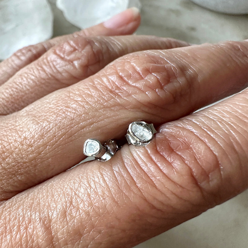 Sterling silver polki diamond stud earrings on finger, round faceted stones with back posts