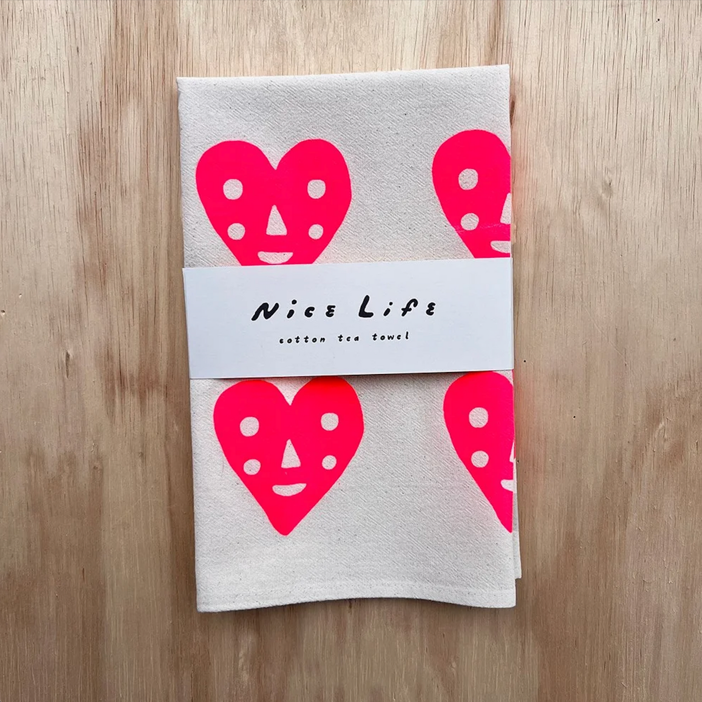 Folded light gray tea towel with pink heart faces and 'Nice Life' label
