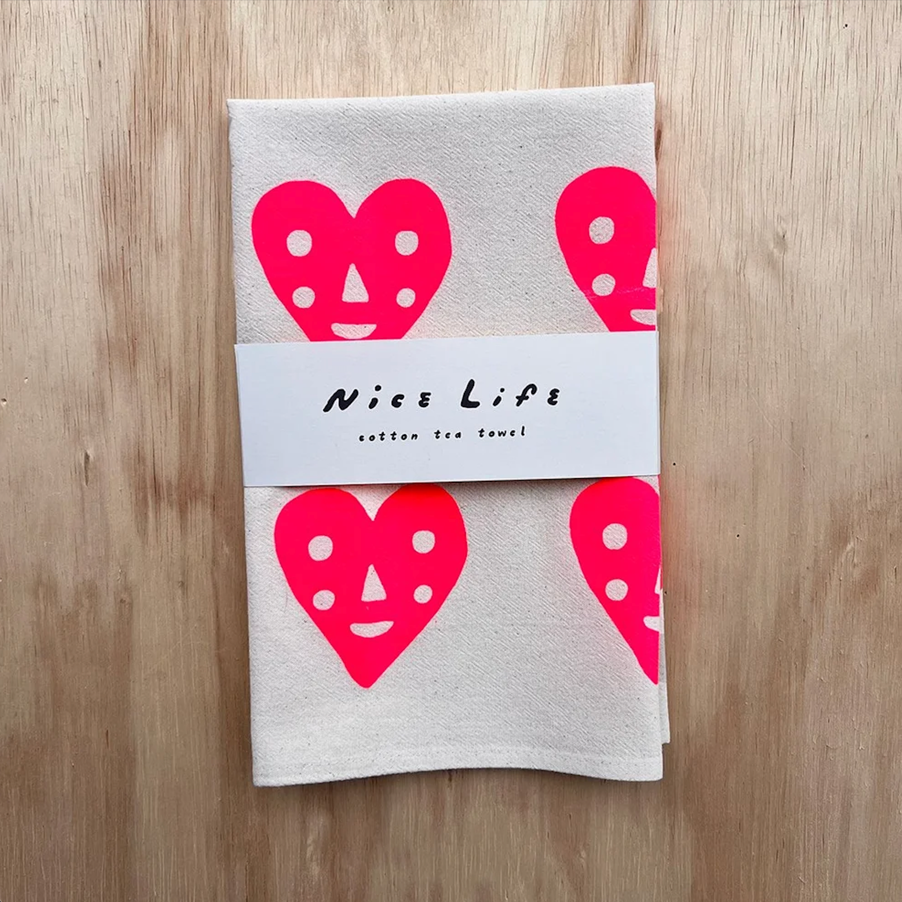 Folded light gray tea towel with pink heart faces and 'Nice Life' label