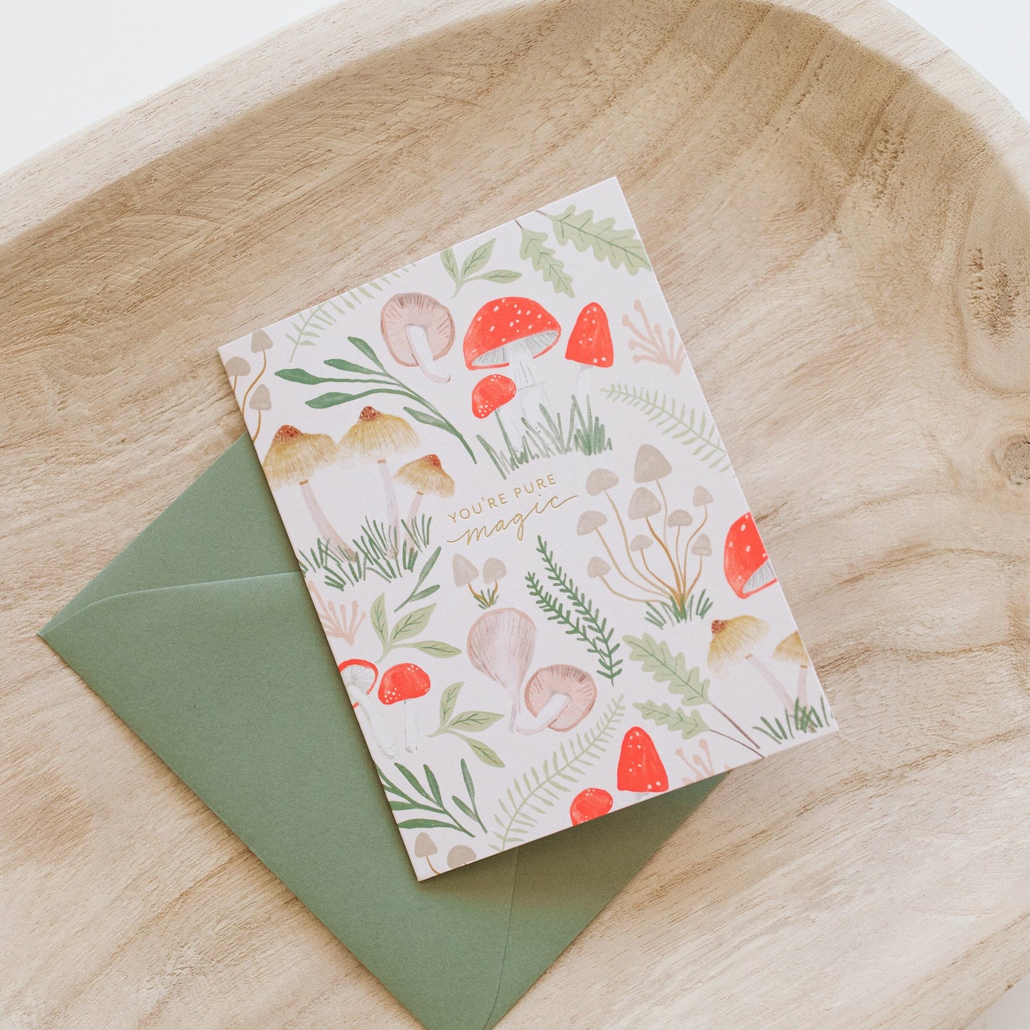 Magic mushroom card on wood with green envelope; red mushroom and green leaf design