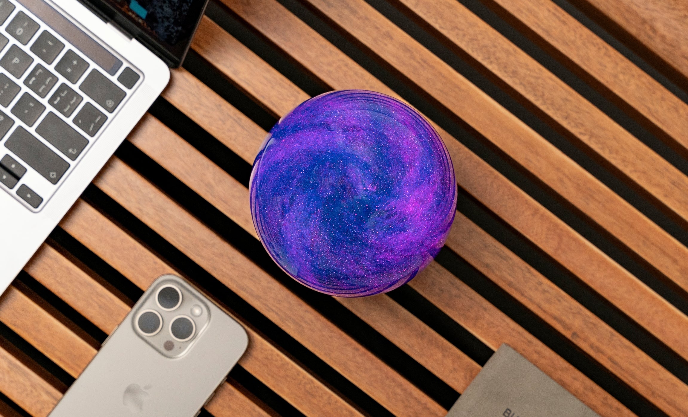 Mini purple swirling glass globe light on dark wooden base, top view