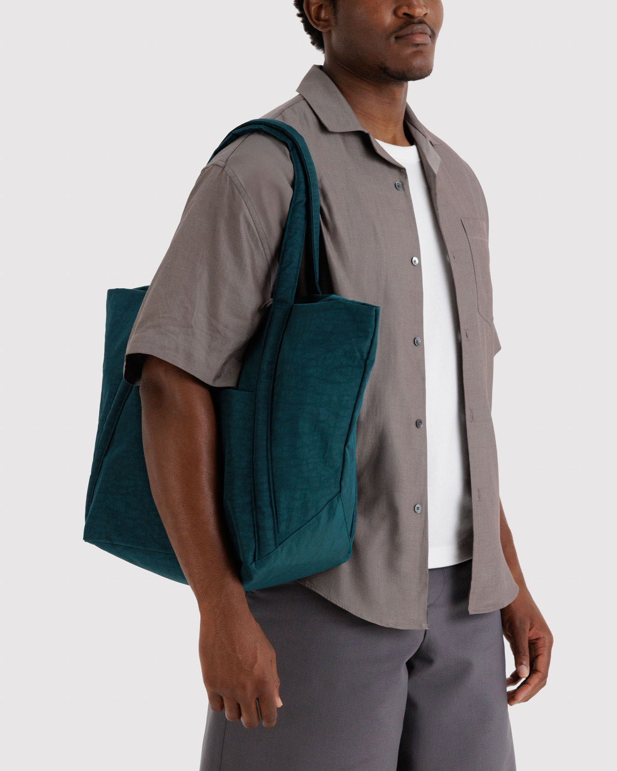 Teal tote bag held at side with two top handles and a structured front pocket.