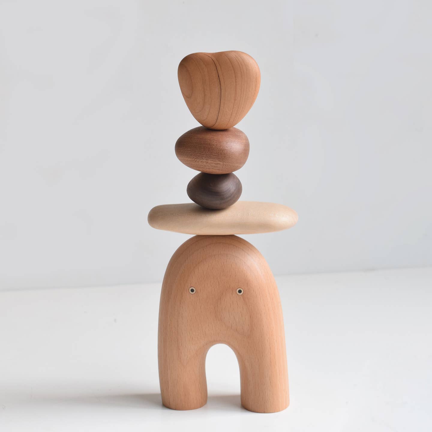 Wooden elf balancing stones figure with stack of round pieces on a seated body