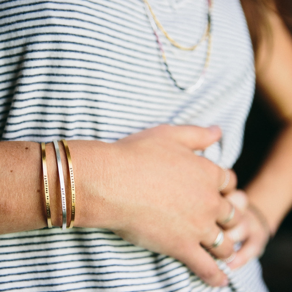 Thin gold cuff bracelet with stamped text, worn on wrist