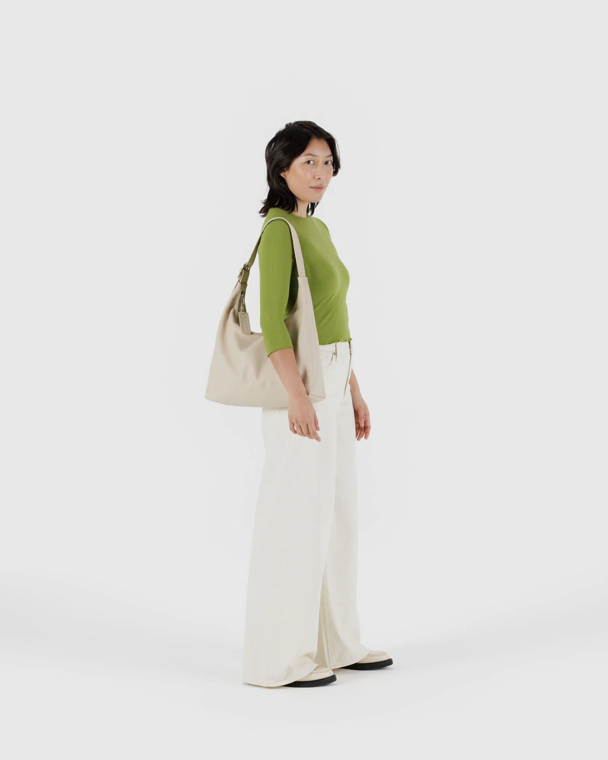 Olive green recycled leather shoulder bag with top handle and hanging charm, worn on model