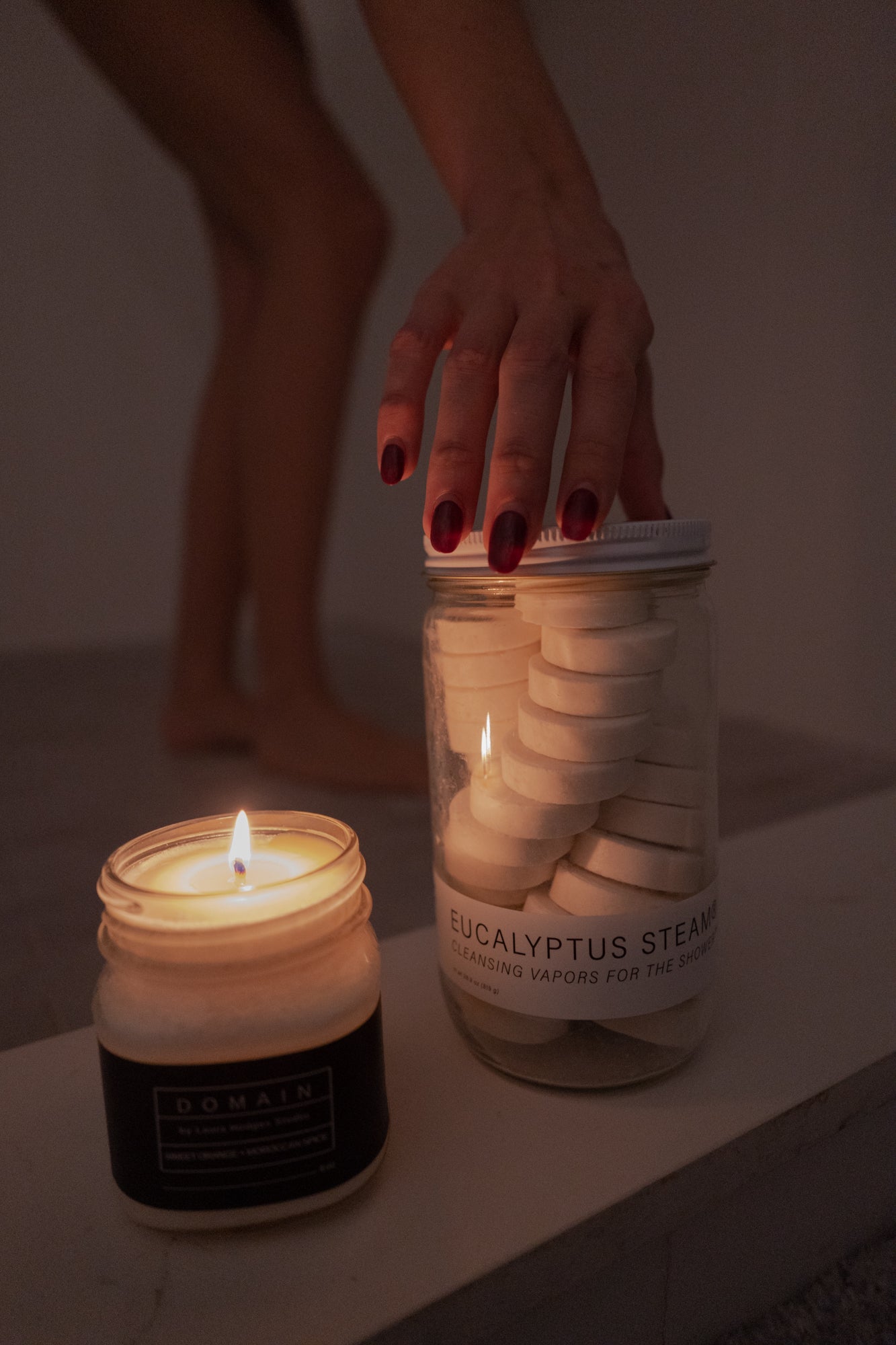 Jar of white shower vapor tablets with an unsealed lid held near a lit candle