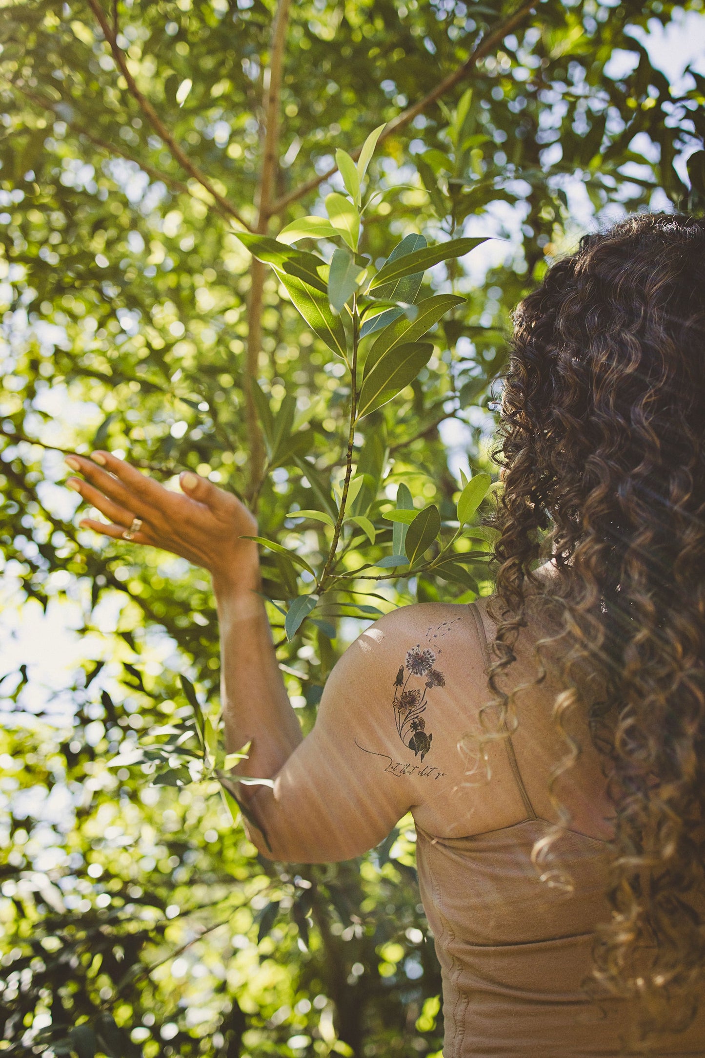 Floral intention tattoo on upper back/shoulder with dandelion design and text.