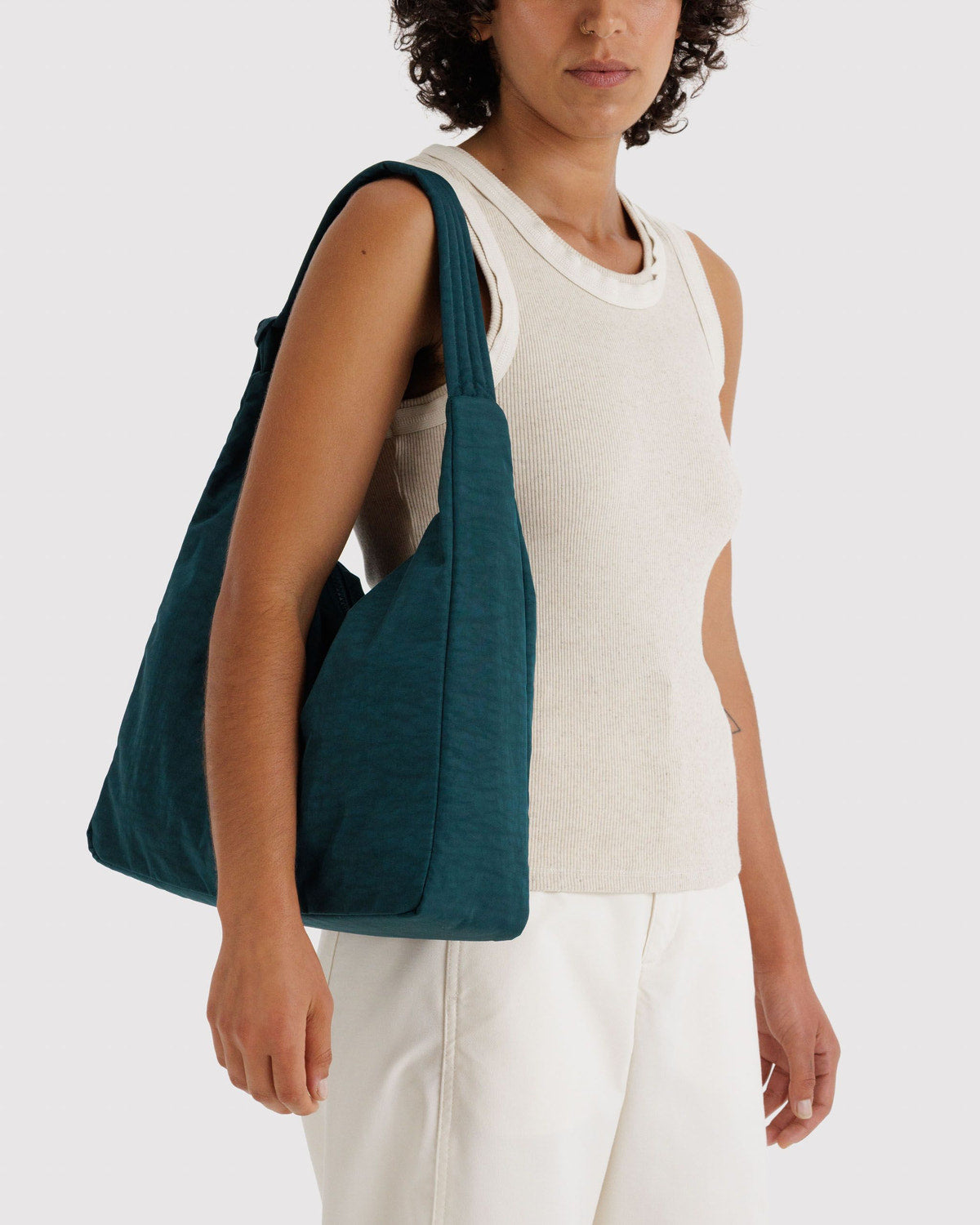Nylon shoulder bag in deep teal green worn crossbody with wide strap and side tie.