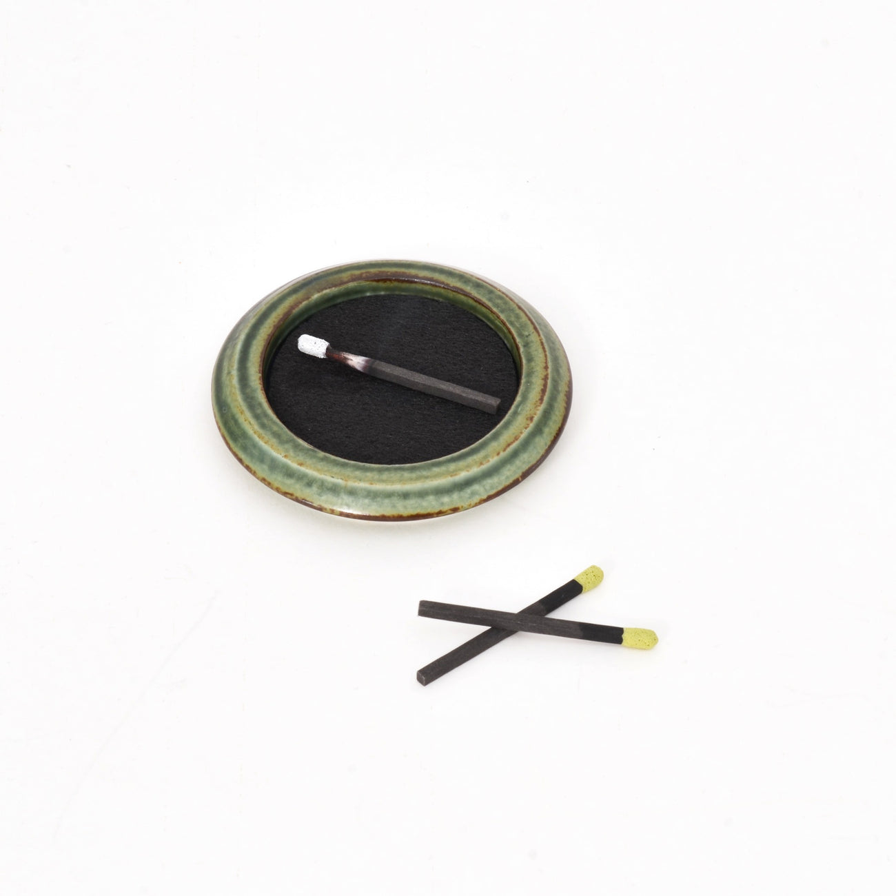 Green ceramic incense tray with black incense pad and two incense sticks