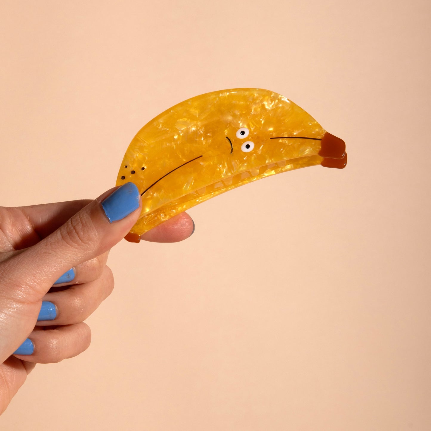 Yellow banana hair claw held by hand, curved clamp with glossy finish