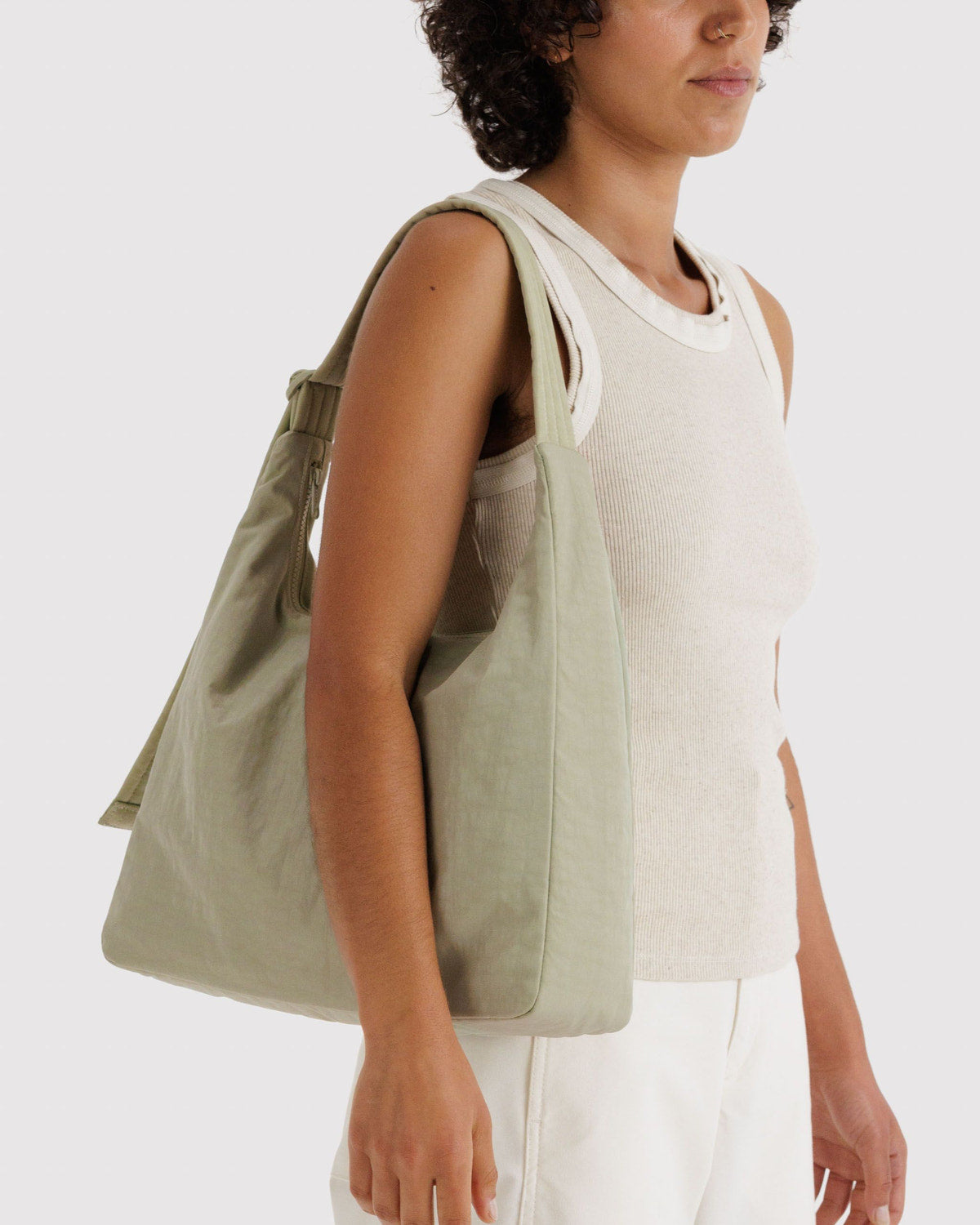 Nylon shoulder bag in light olive green worn crossbody with wide strap and top handle.