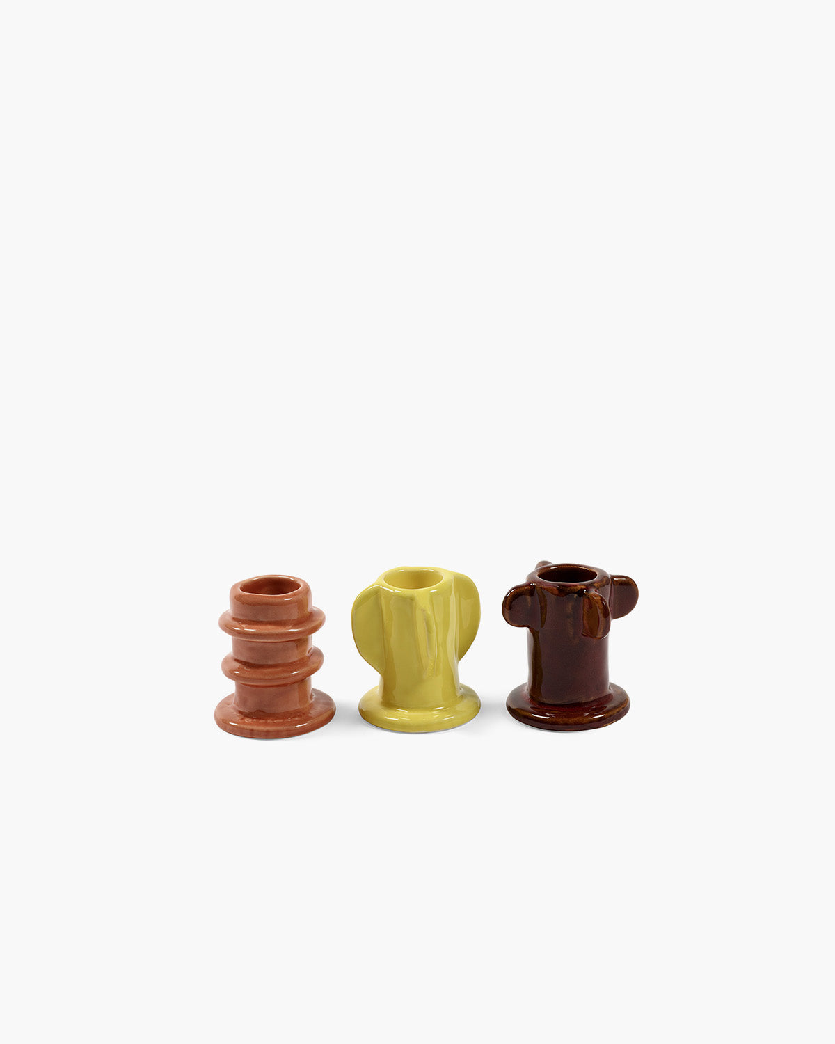 Small glazed candle holders in terracotta, yellow, and dark brown, ring-like base