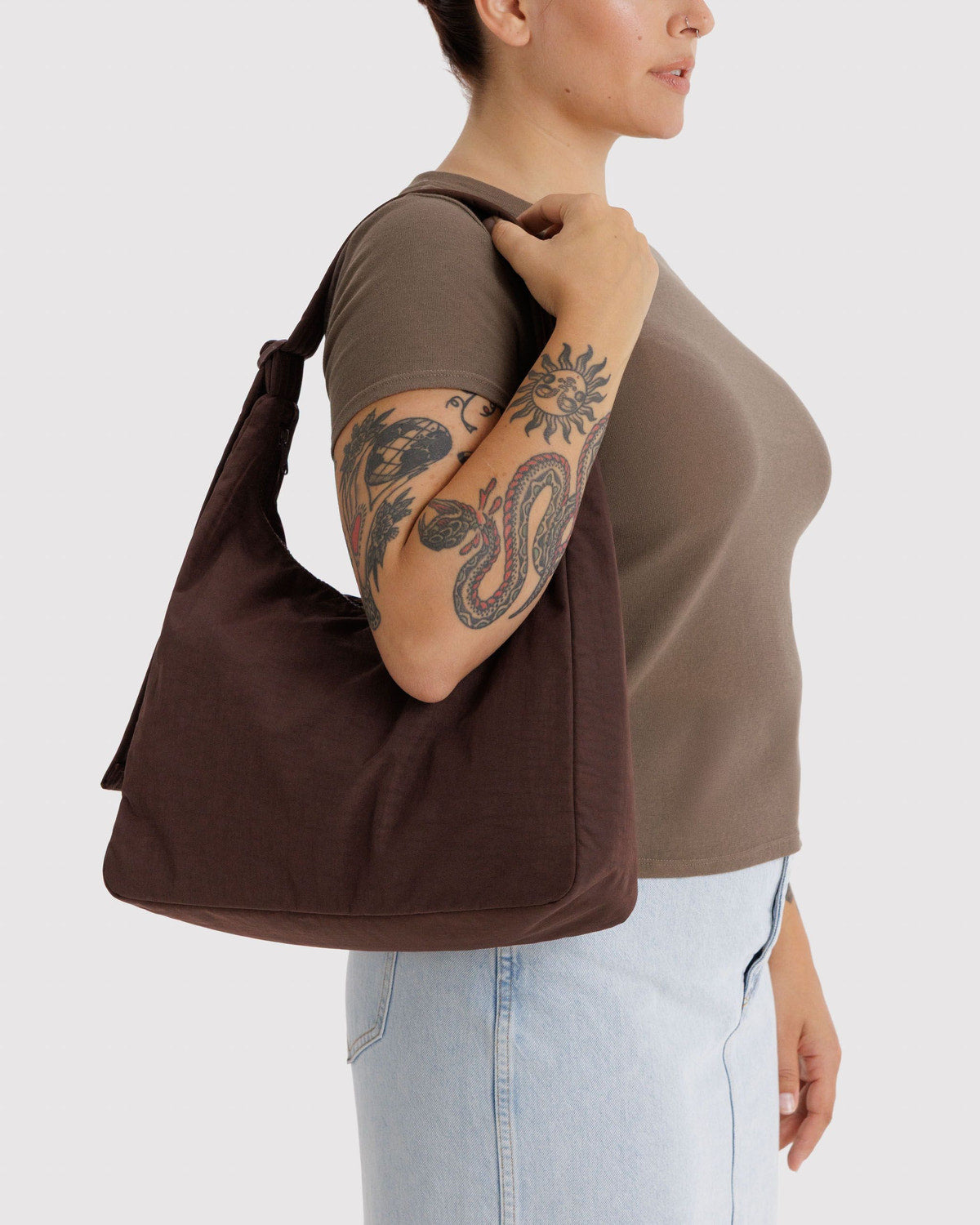 Brown nylon shoulder bag worn on shoulder, with curved handles and tassel