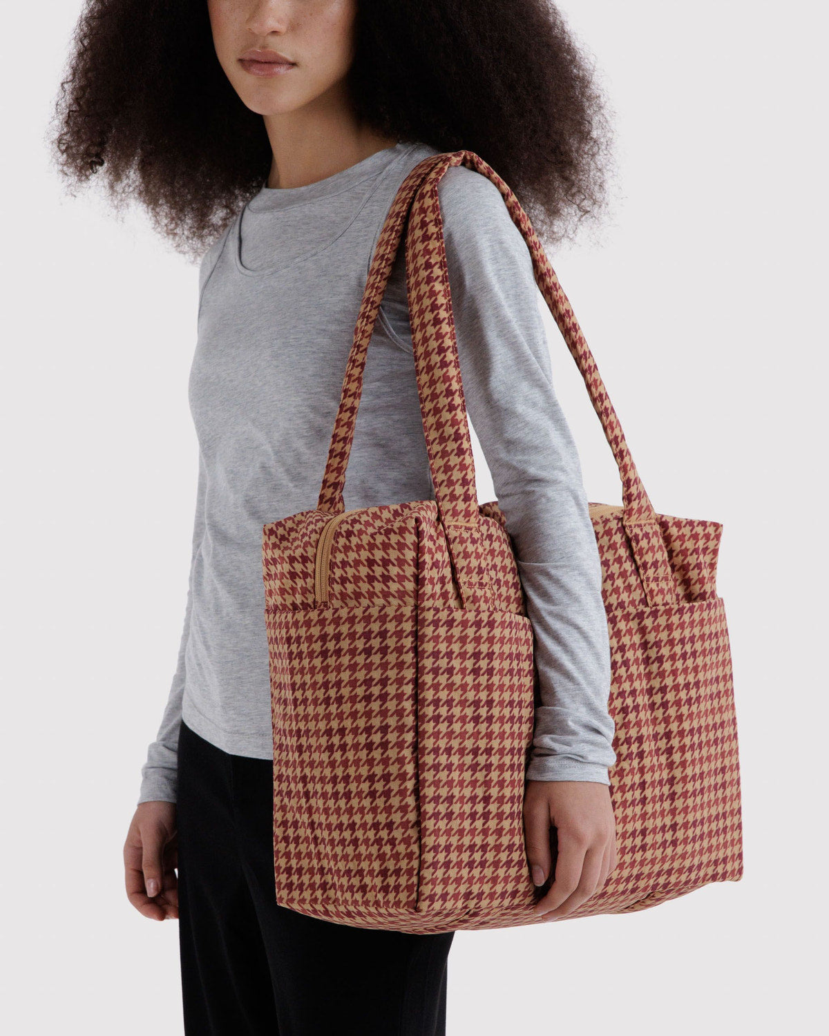 Brown houndstooth foldable tote bag worn over the shoulder with long handles.