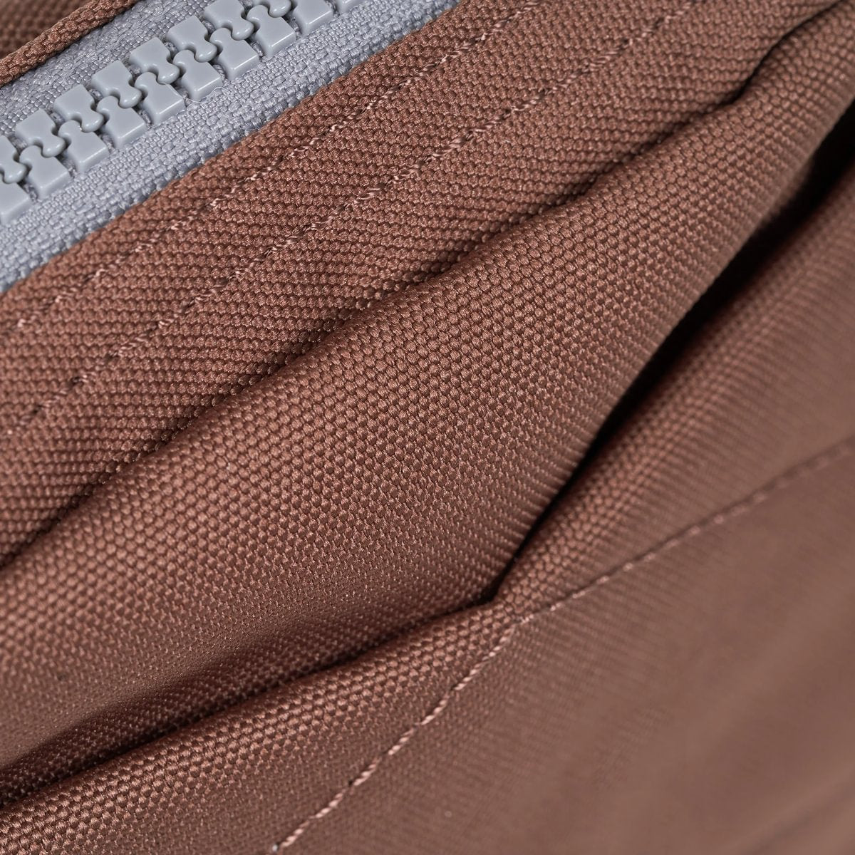 Close-up of brown canvas crossbody bag zipper and textured fabric panel