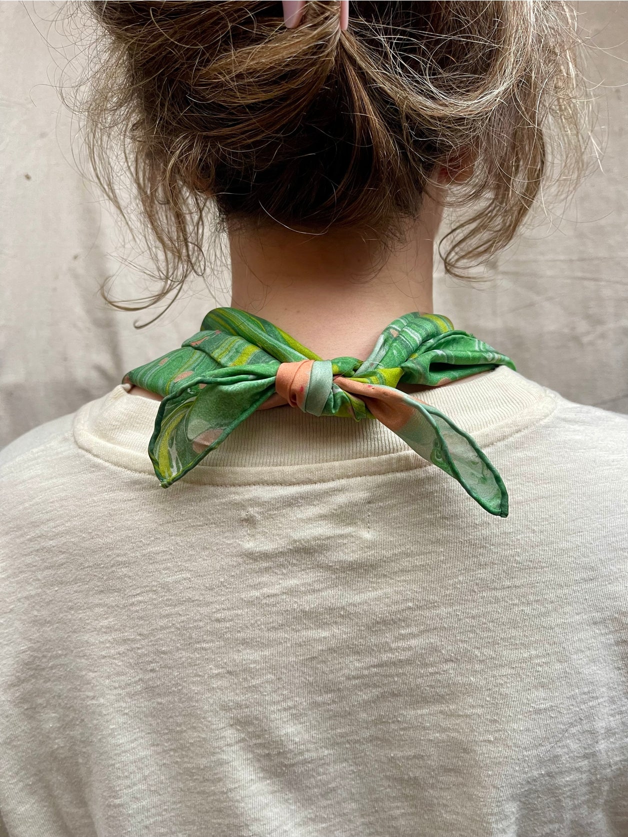 Green silk bandana worn at neck with marbled swirl and dot print, tied bow.