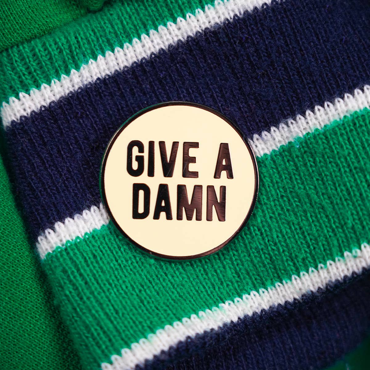 Round enamel pin with 'GIVE A DAMN' text, black lettering, gold rim
