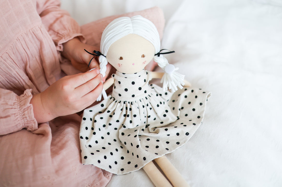 Fabric doll wearing white headscarf and black polka-dot dress as hands adjust it