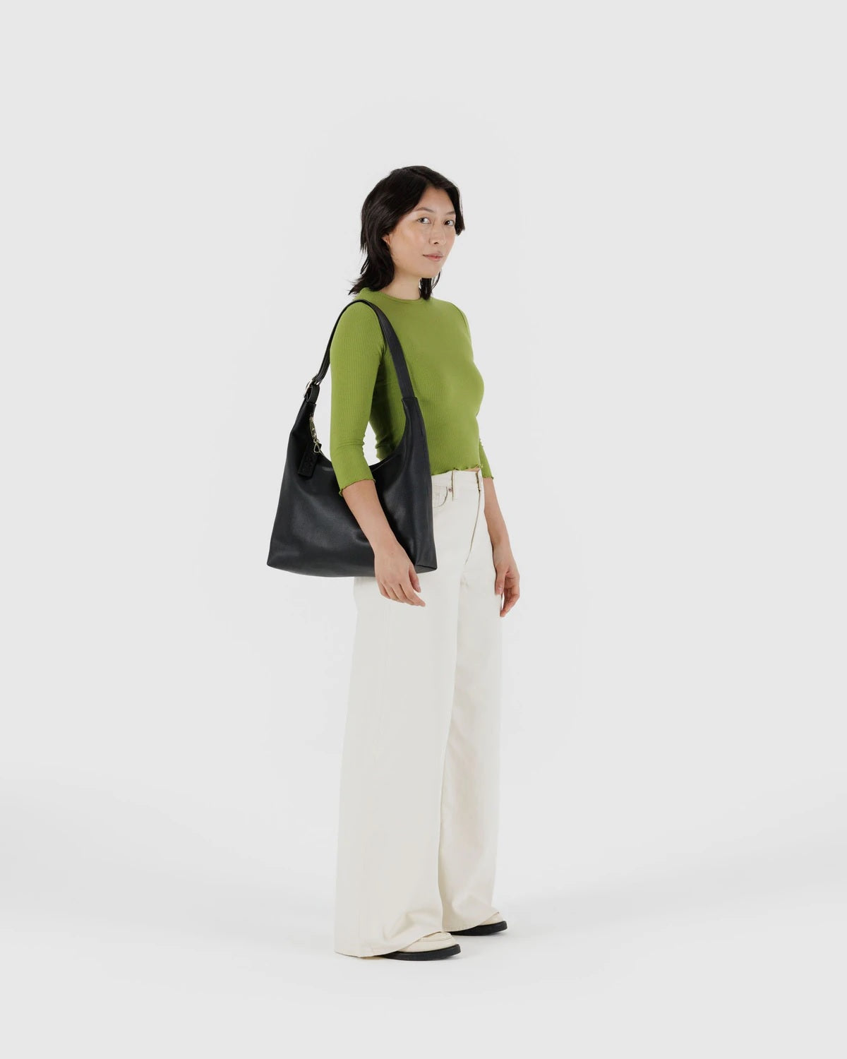 Black recycled leather shoulder bag with top handle and hanging charm, worn on model