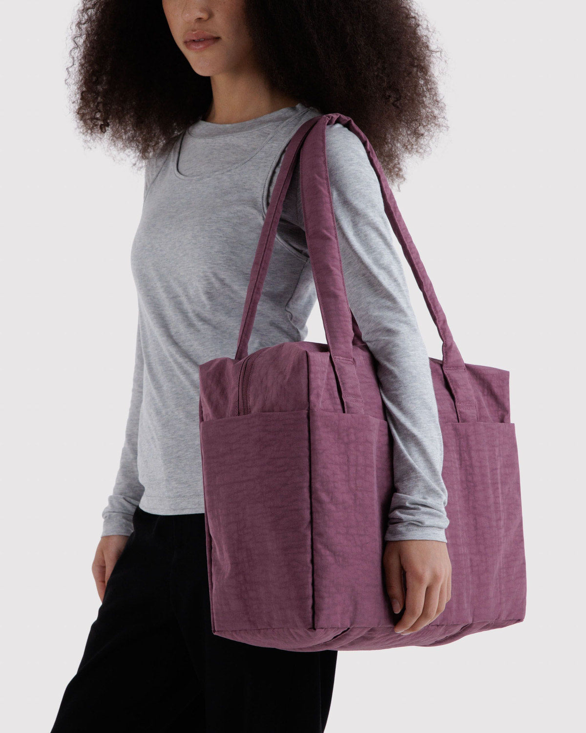 Purple foldable tote bag carried on a person, with long handles and side openings.