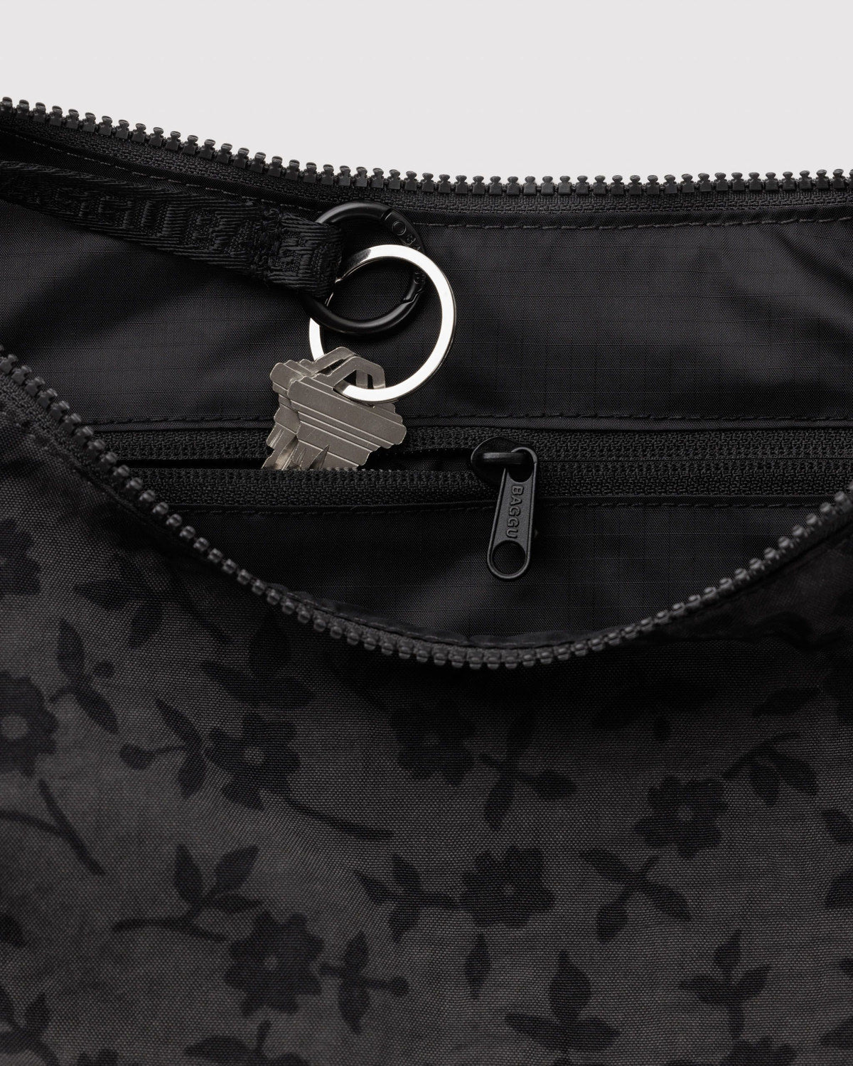 Black nylon crescent bag with top zipper, metal ring pull, and subtle floral print