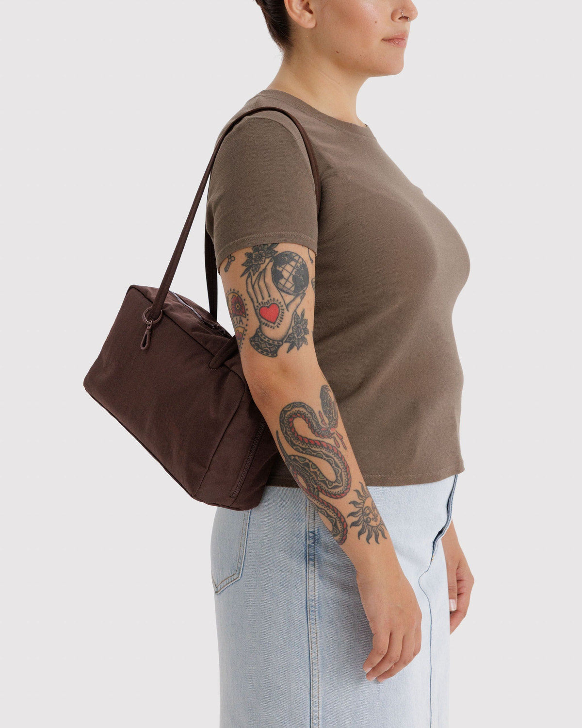 Dark brown nylon bowler bag with top zipper and short handles, carried at side