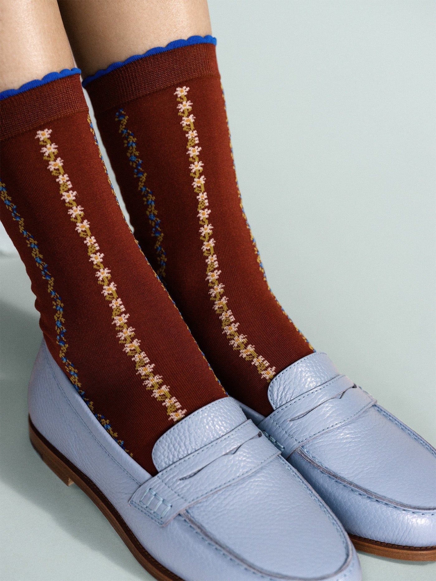 Rust crew socks with blue cuffs and vertical yellow floral stripes, white toes (close-up)