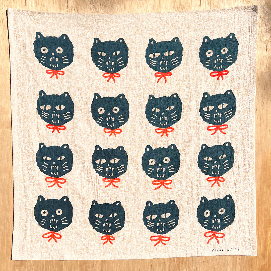 Tea towel with repeating dark cat faces and red bow accents, full-pattern design