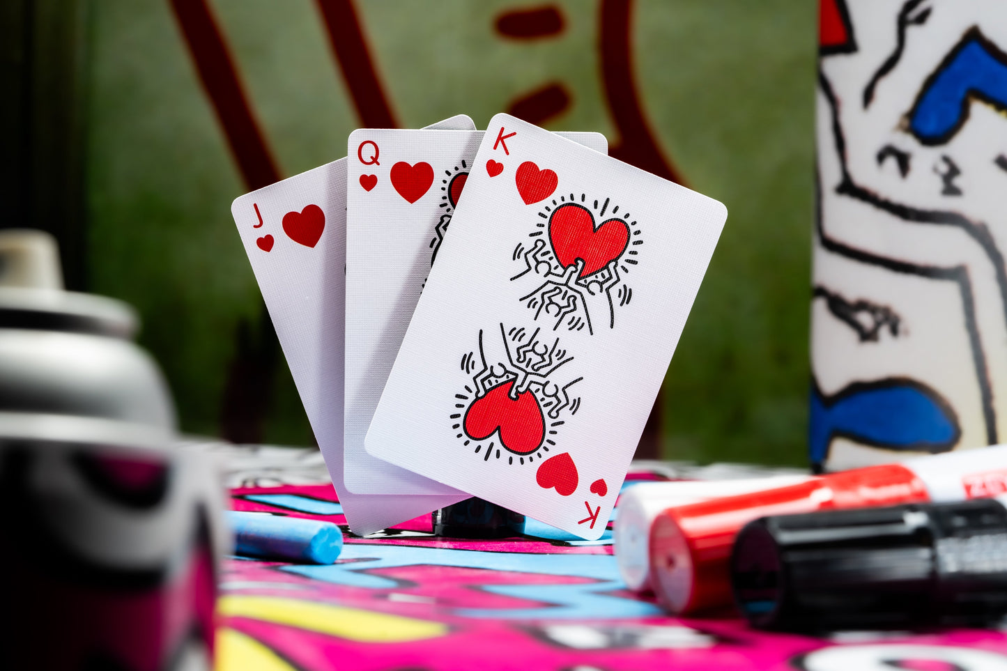 Keith Haring playing cards, three face-up hearts cards on a colorful surface