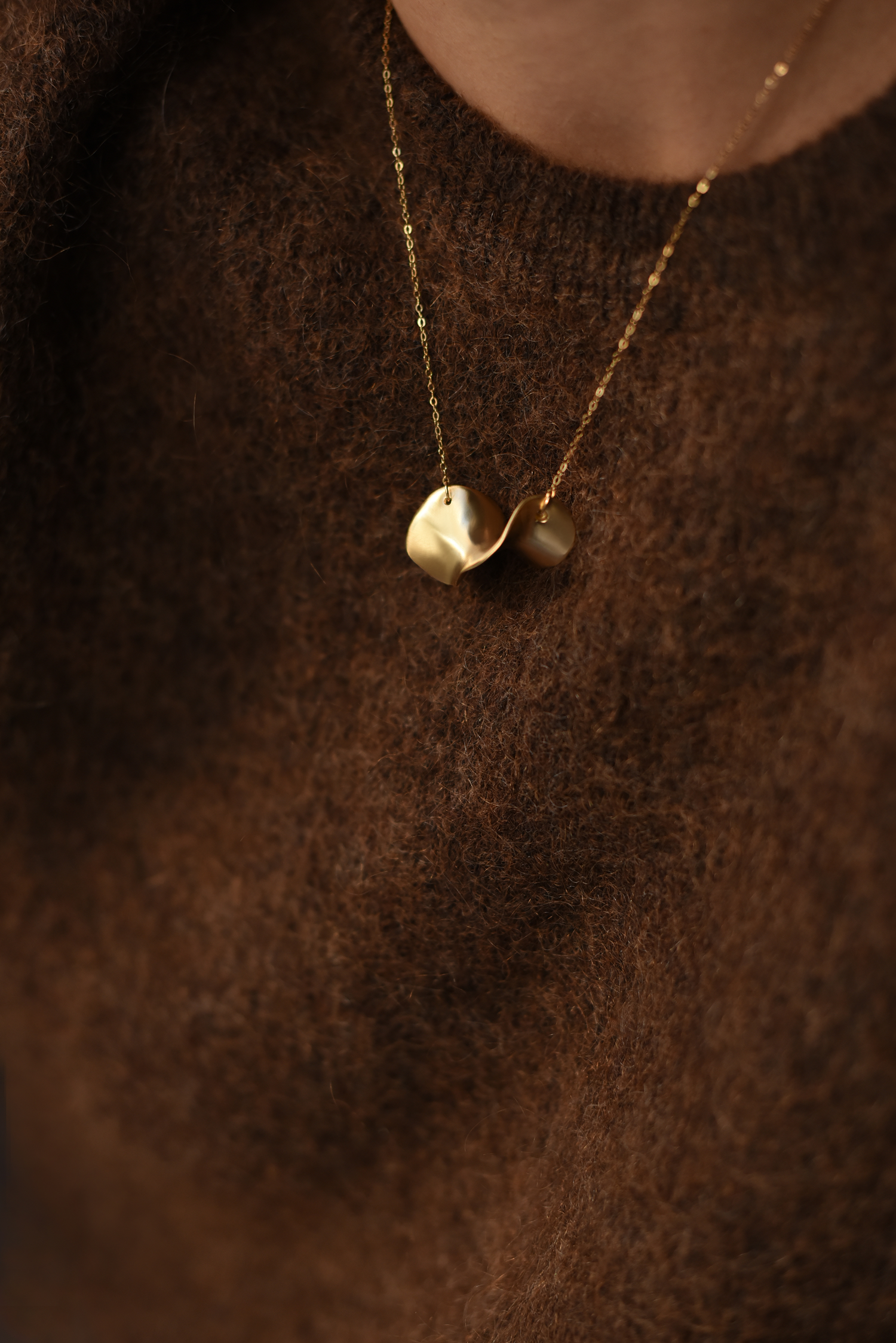 Gold wave brass necklace with curved pendant resting on dark knit sweater