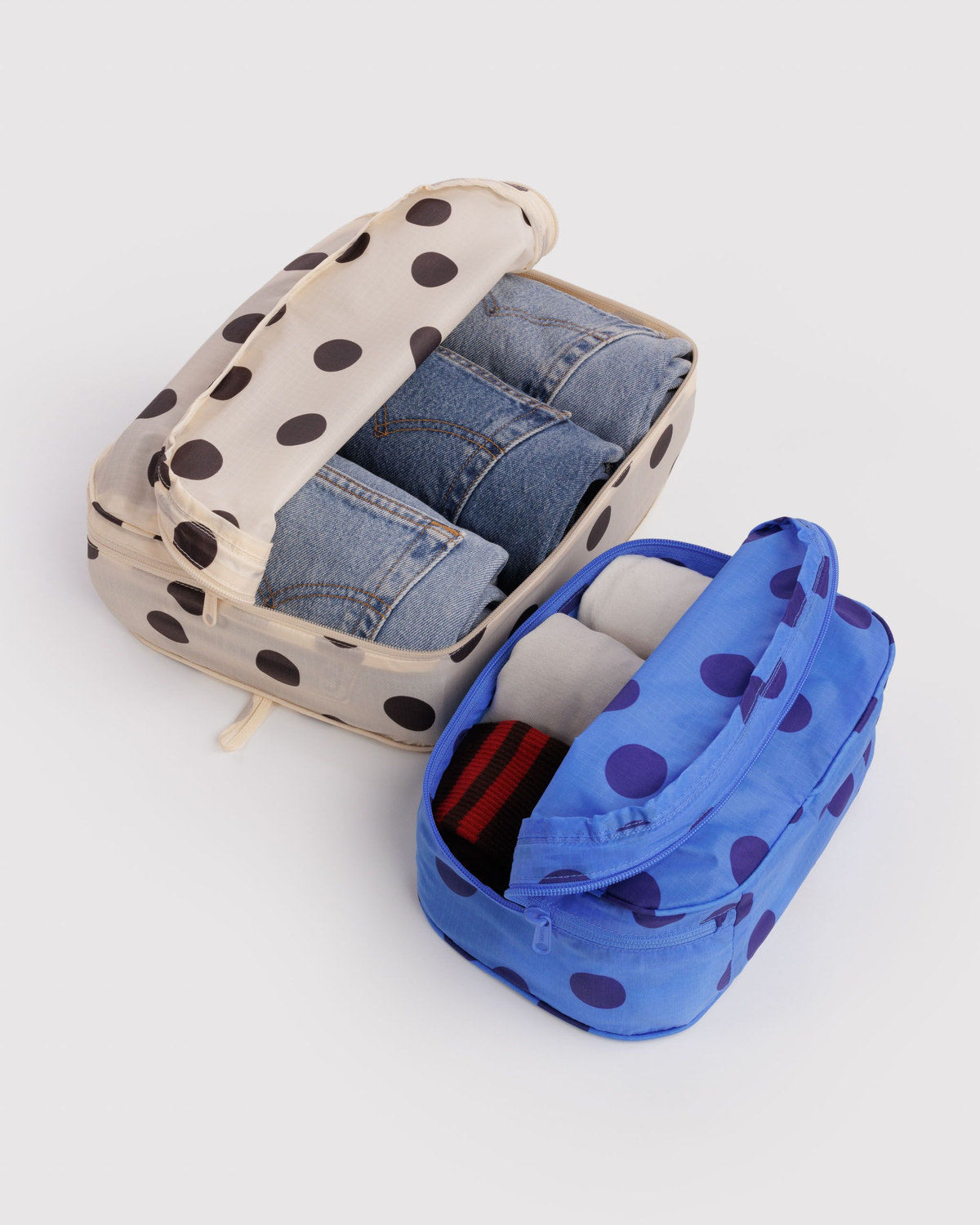 Packing cube set: beige cube and blue polka-dot cube, unzipped with folded denim inside.