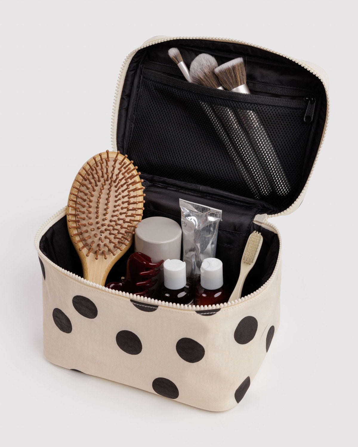 Large cream polka-dot cosmetic case open with brushes and toiletry bottles inside.